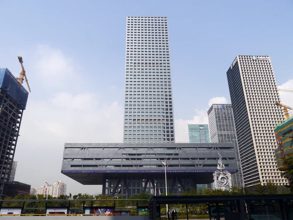 The Shenzhen Stock Exchange: a tall grey tower rising from a wide raised podium, with other office towers beside it.