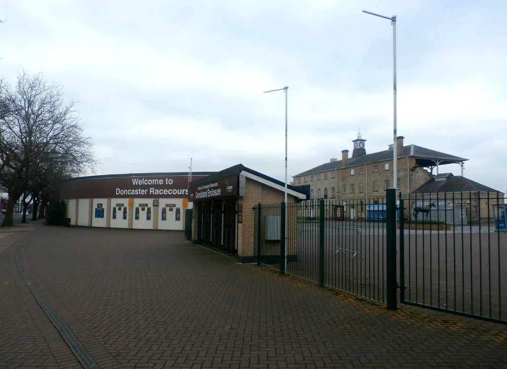 The grandstand entrance and ticket booths of Doncaster Racecourse under a grey sky, with the old clock-towered stand behind.
