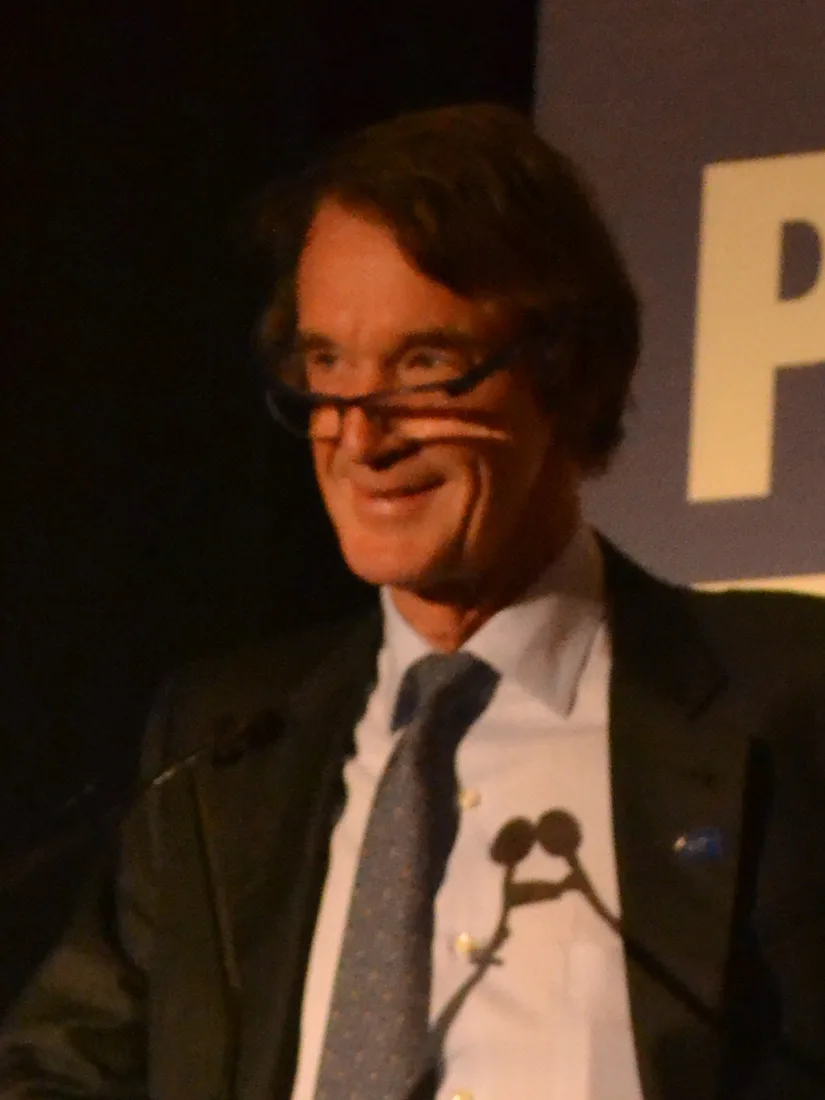 Jim Ratcliffe, in glasses and a dark suit, smiling at a lectern.