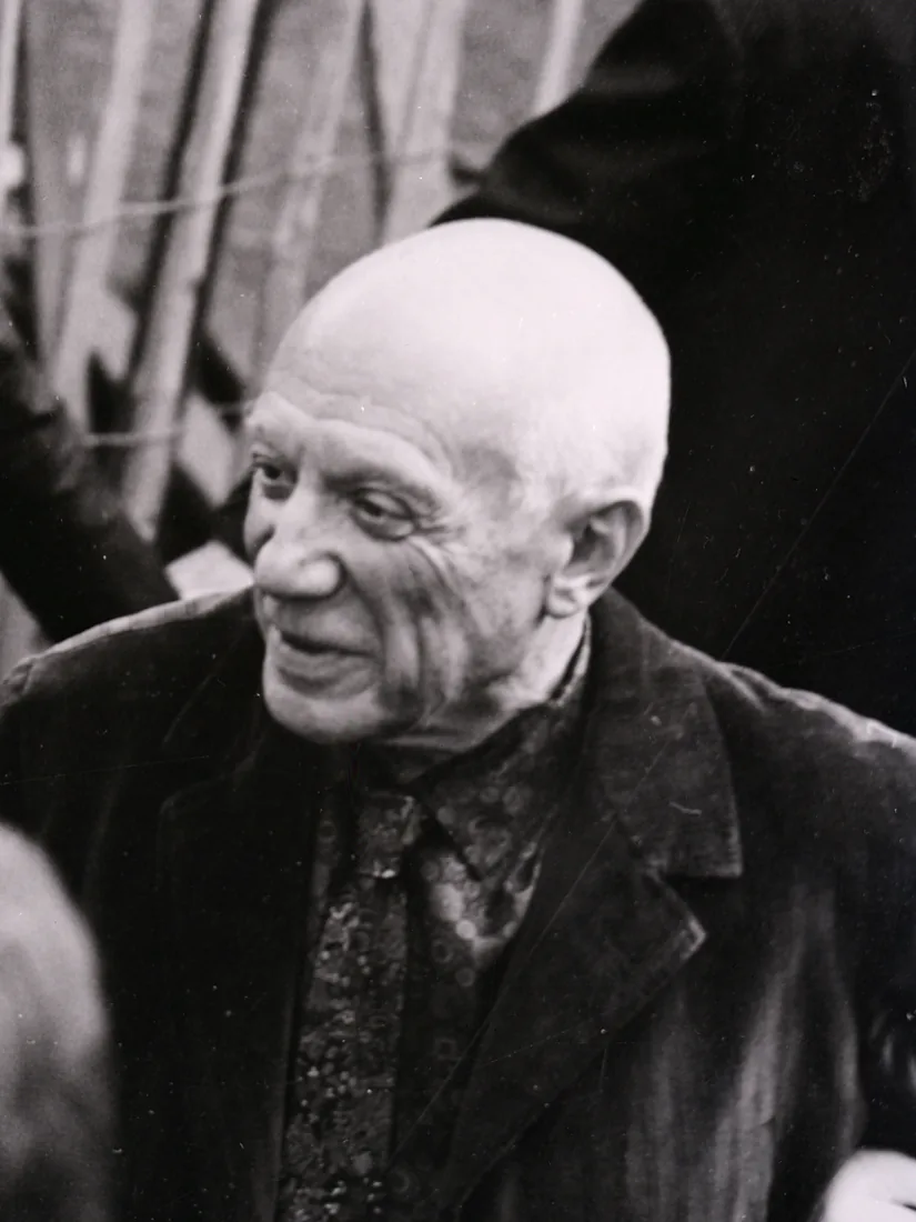 Pablo Picasso in a dark jacket, smiling and looking to one side.