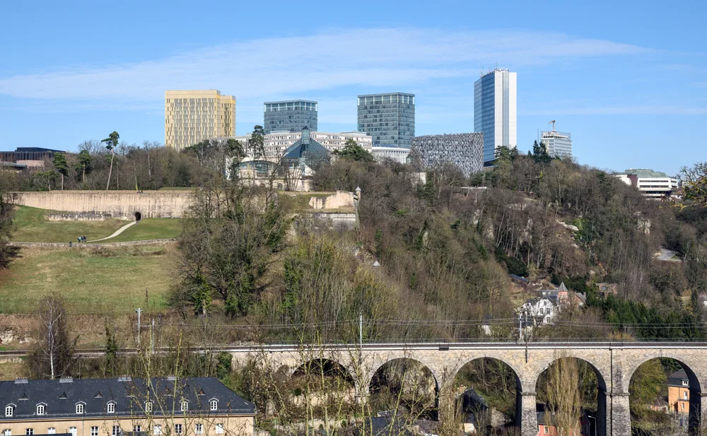 Office towers on a plateau above a wooded valley and a stone railway viaduct.