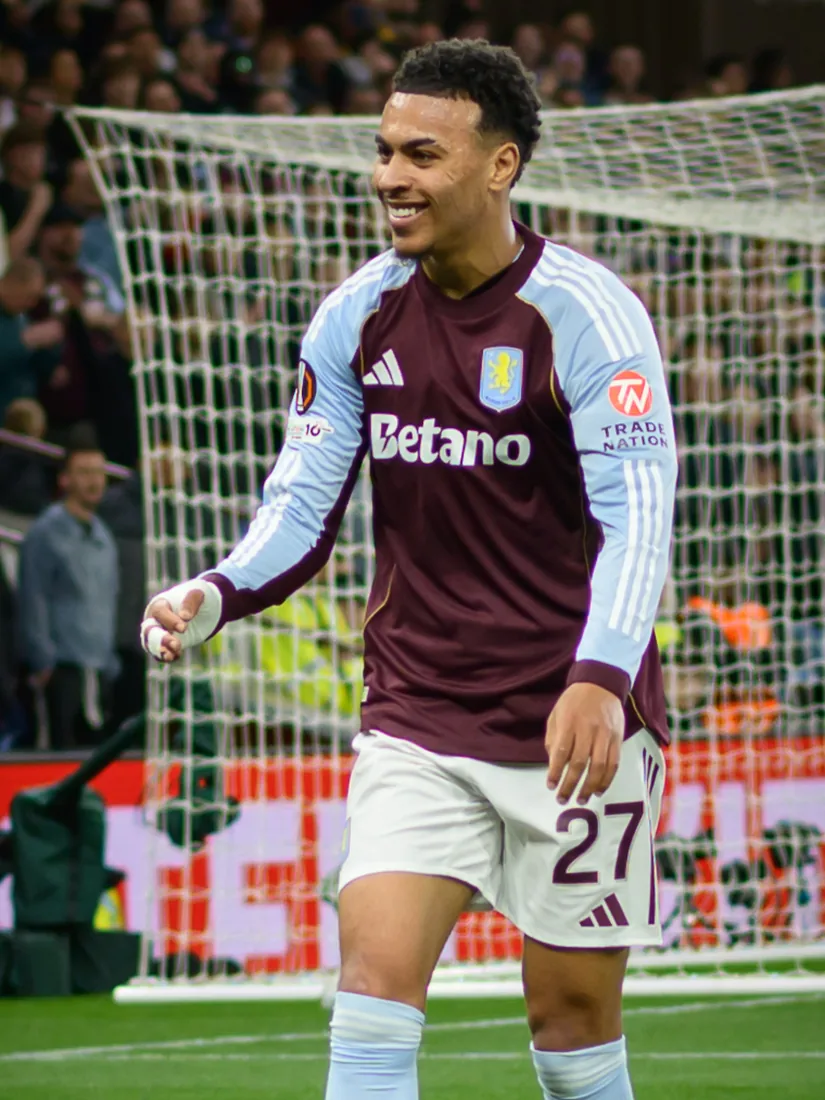Morgan Rogers smiling in an Aston Villa kit in front of a goal net.