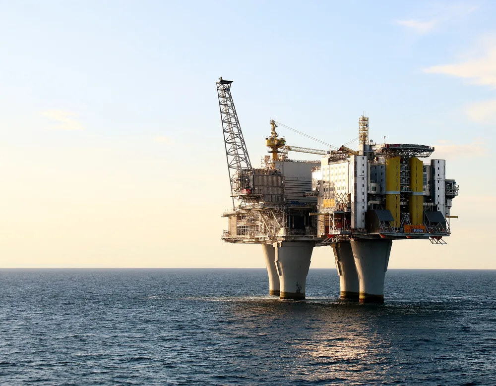 A large offshore platform standing on four concrete legs in a calm sea under a pale sky.