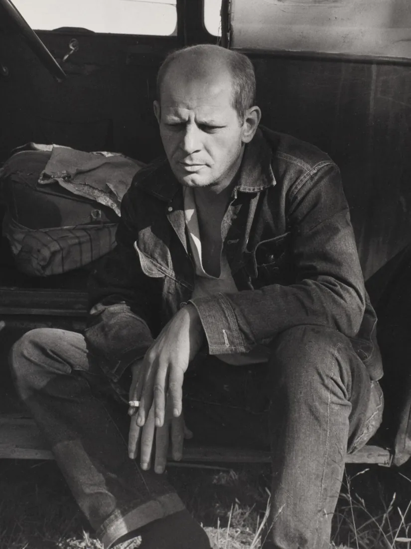 Jackson Pollock sitting in the open doorway of an old car.