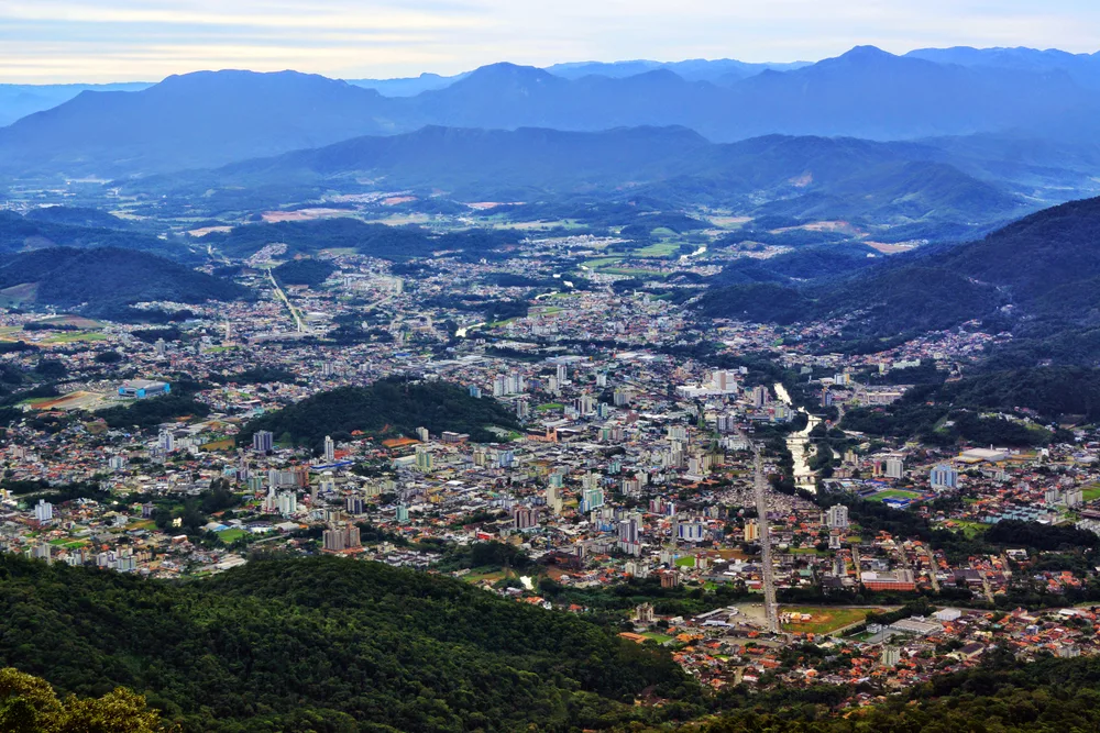 A wide view over a city spread across a green valley, ringed by forested hills and mountains.