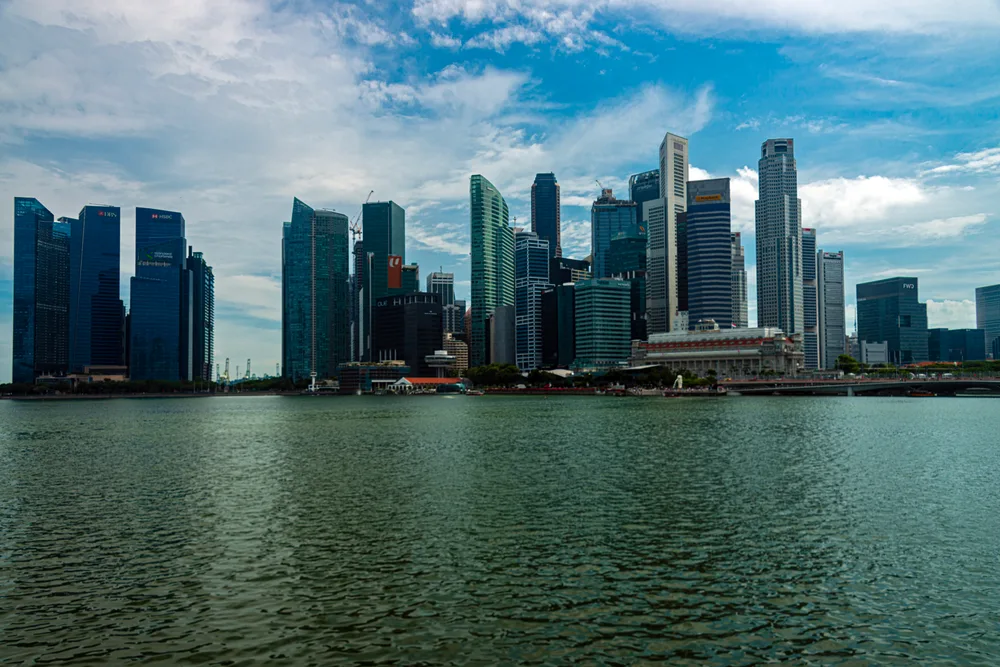 Glass office towers of a financial district lining the far shore of a wide bay under a cloudy sky.