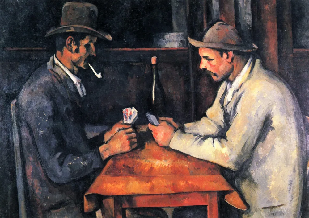 Two men in hats sit facing each other across a table, playing cards.