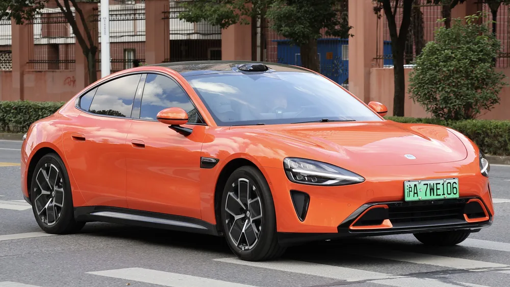 An orange Xiaomi SU7 saloon on a street in Shanghai.